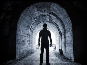 Je ziet een silhouet van een angstige man in een donkere tunnel