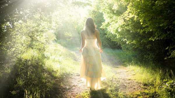 Een vrouw met hooggevoeligheid en hoogsensitiviteit loopt in een witte zomerjurk door een mooi bos