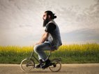 Een hipster met een baard fietst op een heel klein fietsje. Hij heeft alle onzekerheden in zijn onderbewuste opgelost en durft zichzelf te zijn.