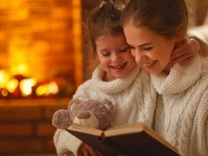 Een moeder met een herfstdepressie heeft haar kind op schoot, ze leest een boek voor, bij de open haard. heerlijk warm en knus.
