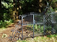 Een zwart gietijzeren hek sluit een pad af, hoewel je er ook langs kunt lopen.