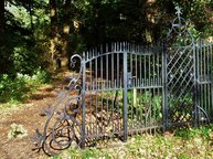 Een zwart gietijzeren hek sluit een pad af, hoewel je er ook langs kunt lopen.