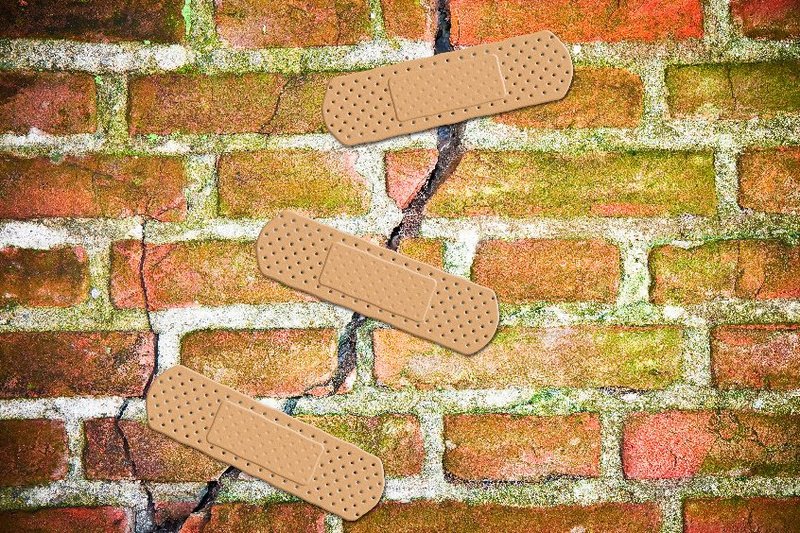 Een muur met een trauma: een bakstenen muur met een grote barst erin. Drie pleisters zijn over de barst geplakt.