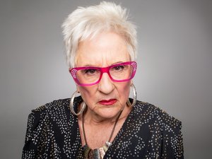 Een oudere narcistische vrouw met een rode bril op kijkt afkeurend, dwingend