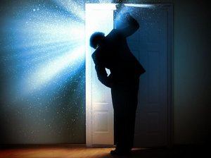 In een donkere kamer gluurt een man achter een deur die op een kier staat. In de ruimte achter de deur is het licht.