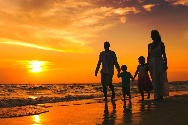 Een gezin dat een kind heeft verloren loopt met nog maar 2 kinderen op het strand, bij een ondergaande zon