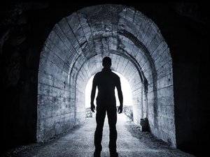 Je ziet een silhouet van een angstige man in een donkere tunnel