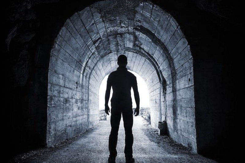 Je ziet een silhouet van een angstige man in een donkere tunnel