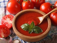 Een bord heerlijke tomatensoep op een tafel, met daar omheen verse tomaten en knoflook