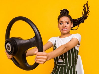 Een vrouw met rijangst kijkt angstig en houdt een autostuur in de handen, tegen een gele achtergrond