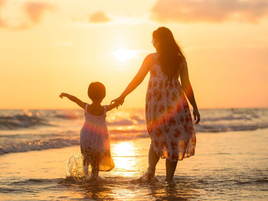 een herinnering van een moeder met haar kind aan de hand, aan het strand bij een ondergaande zon.