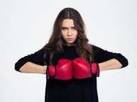 Een jonge vrouw met rode bokshandschoenen drukt haar handen boos tegen elkaar, en ze kijkt boos