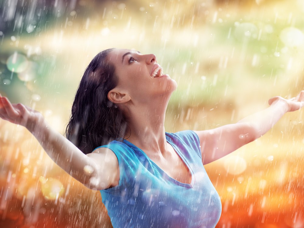 Een vrouw geniet als een kind, ze spreidt haar armen en kijkt omhoog om de regen in haar gezicht te voelen.