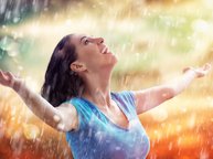 Een vrouw geniet als een kind, ze spreidt haar armen en kijkt omhoog om de regen in haar gezicht te voelen.