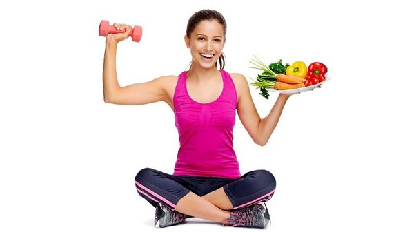 Een vrouw in sportkleding zit in kleermakerszit. In de ene hand een gewicht, in de andere een bord gezonde voeding.