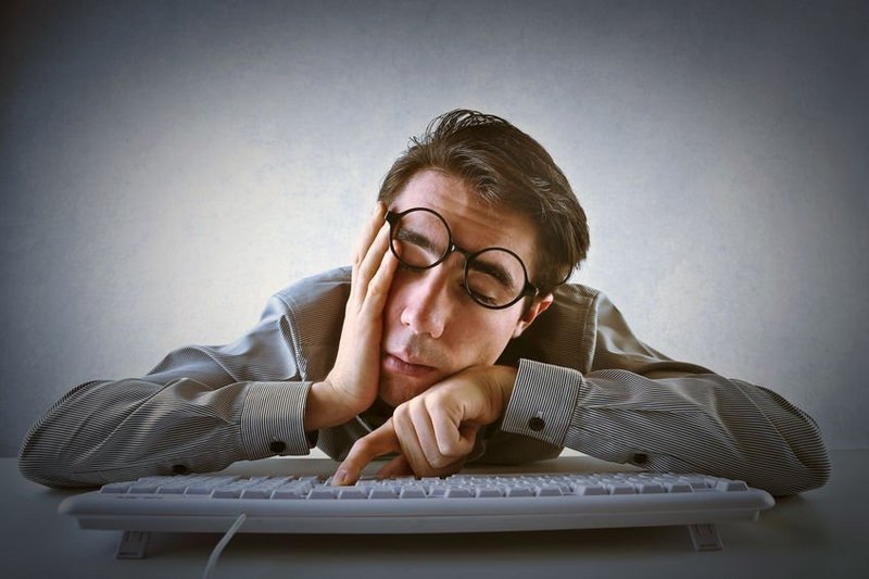 Een man hang doodmoe over zijn laptop, hij heeft energiegebrek door een blokkade in het energieveld