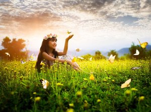 Hooggevoelig meisje zit in een veld vol bloemen en vlinders. Ze heeft een krans van bloemen om haar hoofd, en een vlinder landt op haar hand.