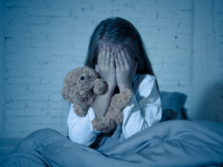 Een kindje is bang voor geesten en zit met haar handen voor haar ogen in bed. Ze wil de geesten niet meer zien.