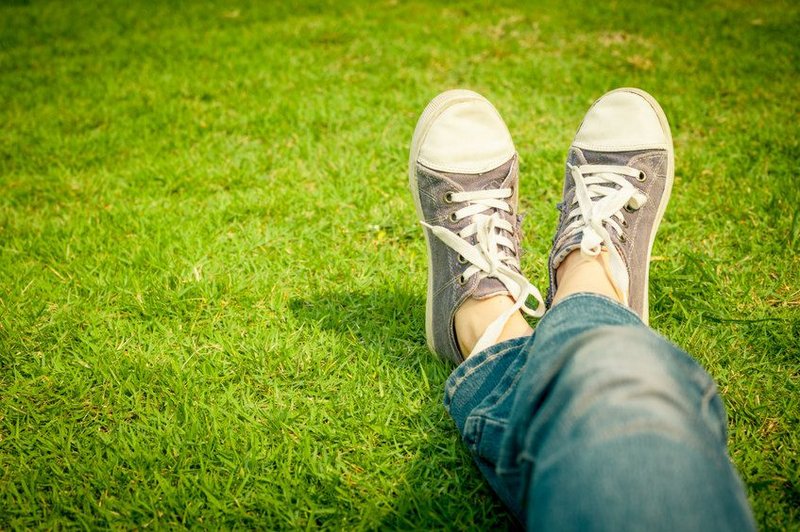 Je ziet twee koude voeten met gymschoenen aan, in het gras. Alsof je zelf op het gras ligt, alsof het jouw voeten zijn.