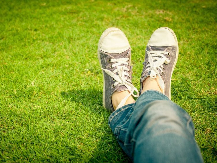 Je ziet twee koude voeten met gymschoenen aan, in het gras. Alsof je zelf op het gras ligt, alsof het jouw voeten zijn.