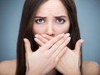 Een vrouw heeft spontaan iets fout gezegd en houdt met spijt haar handen voor haar mond.