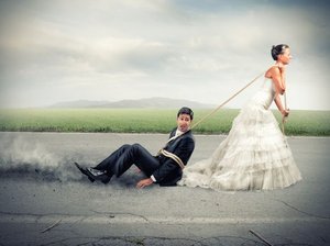 Een bruid in trouwjurk sleept haar kersverse echtgenoot over het asfalt. Zij moeten leren communiceren in hun relatie.