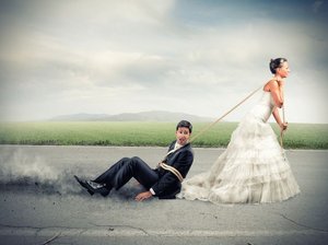 Een bruid in trouwjurk sleept haar kersverse echtgenoot over het asfalt. Zij moeten leren communiceren in hun relatie.