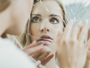 Een vrouw kijkt onzeker in een gebarsten spiegel