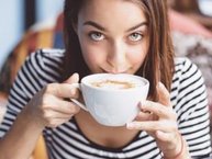 Een vrouw drinkt een grote kop cappuccino, en kijkt een beetje twijfelachtig. Ze is hooggevoelig en hoogsensitief.