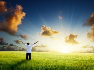 Een man staat in het gras te genieten van de opkomende zon.