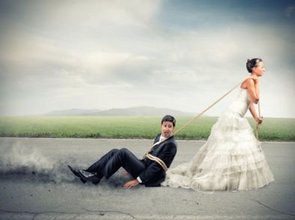 Een bruid in trouwjurk sleept haar kersverse echtgenoot over het asfalt