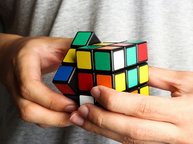 Twee handen proberen een Rubic's cube op te lossen.