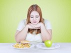 Een mooie vrouw steunt met de handen onder het hoofd. Ze twijfelt tussen de appel of het bord met hamburger en frites. Ze probeert haar dieet in evenwicht te houden.