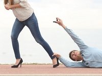 Een stel met relatieproblemen. De vrouw loopt weg maar de man sleept over de vloer, hangend aan haar enkel, terwijl hij een trouwring aan haar aanbiedt.