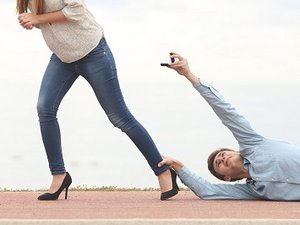 Een stel met relatieproblemen. De vrouw loopt weg maar de man sleept over de vloer, hangend aan haar enkel, terwijl hij een trouwring aan haar aanbiedt.