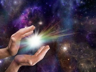 De geboorte van het licht: twee handen bevrijden een stralend lichtje, tegen een donkere sterrenhemel.