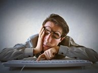 Een man met energiegebrek valt bijna in slaap op zijn laptop, met 1 vinger op het toetsenbord en de ogen al dicht
