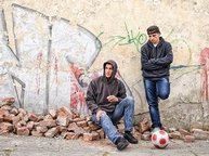 Twee pubers hangen verveeld tegen een muur met graffity.