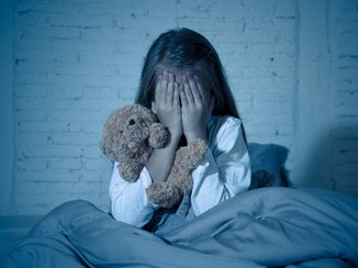 Een kindje is bang voor entiteiten en zit met haar handen voor haar ogen in bed. Ze wil de entiteiten niet meer zien.