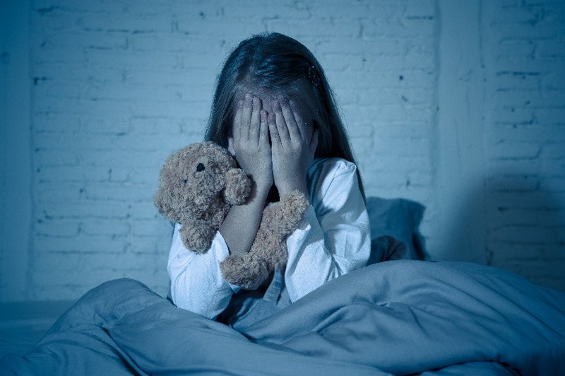 Een kindje is bang voor geesten en zit met haar handen voor haar ogen in bed. Ze wil de geesten niet meer zien.