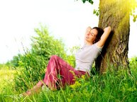 Een vrouw ligt in het gras tegen een boom te genieten van het mooie weer