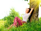 Een vrouw ligt blij in het gras tegen een boom te genieten van het mooie weer