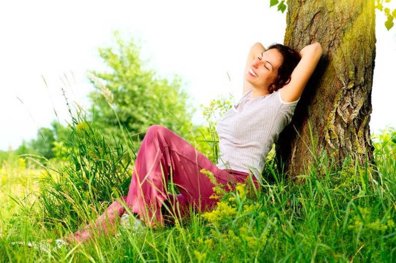Een vrouw ligt in het gras tegen een boom te genieten van het mooie weer