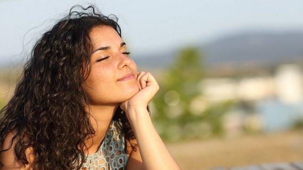 Een HSP vrouw geniet door haar hoogsensitiviteit intens van de zon op haar gezicht in een prachtige omgeving.