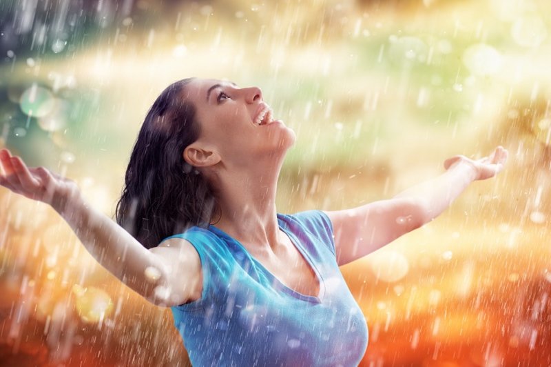Een vrouw staat helemaal blij te genieten van de regen