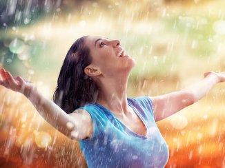 Een vrouw staat helemaal blij te genieten van de regen.