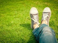 Je ziet twee voeten met gymschoenen in het gras, alsof je zelf op het gras ligt, alsof het jouw voeten zijn.