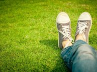 Je ziet twee voeten met gymschoenen in het gras, alsof je zelf op het gras ligt, alsof het jouw voeten zijn.