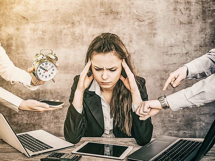 Een vrouw achter een bureau is burn-out, mensen om haar heen wijzen op de klok, en zetten haar onder druk.