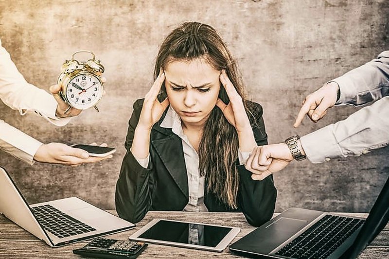 Een vrouw achter een bureau is burn-out, mensen om haar heen wijzen op de klok, en zetten haar onder druk.